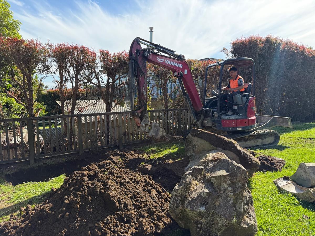 Mini digger excavating a damaged drain line for replacement at a South Auckland residential property
